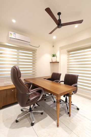 The L-shaped desk from nearer, a ceiling fan above and a table on turned legs running out from it.