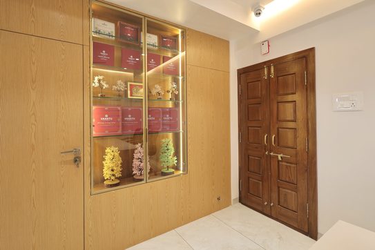 A lit glass display case set into a wood-grain wall, a flush door beside it and a dark panelled double door in the corner.