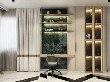 A lit display and shelving unit in pale stone and brass, either side of a green marble panel, with a desk in front of it.