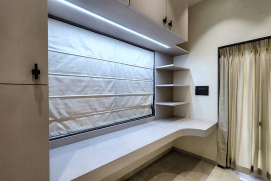 A curved timber shelf niche built into the corner beside a bed, under a window blind.