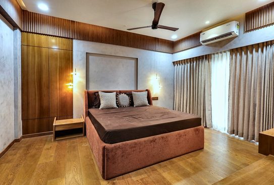 A bed upholstered in rust velvet against a teak-panelled wall, with a wall light beside it and long curtains behind.