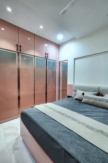 Glossy pink wardrobe fronts along one wall of a bedroom, with a bed in front of them.